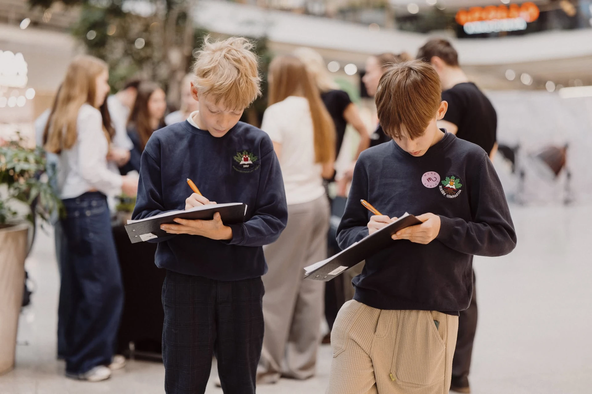 Two young students taking notes on clipboards during an expo